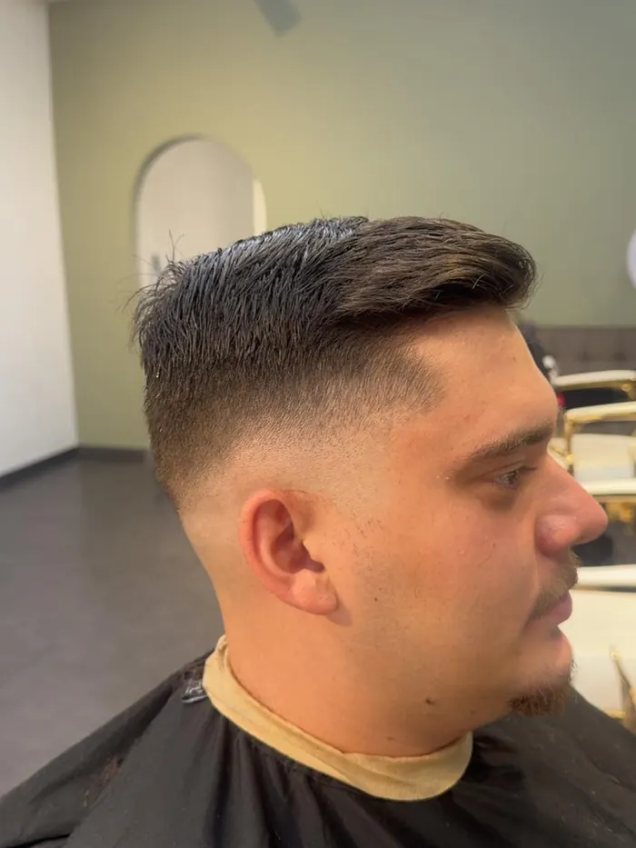 Herrenschnitt, hoher Fade an der Seite, längeres Deckhaar nach hinten frisiert.